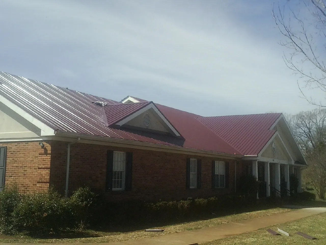 Red metal roof with gabled entries on a long brick building, from a Hail Damage Roof Repair job in Millry