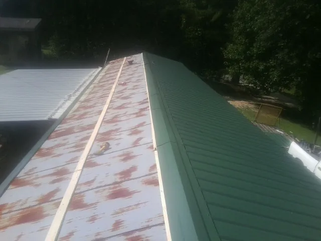 Old rusted panels beside newly installed green metal roofing — Wind Damage Roof Repair by Roofing Brothers in Millry
