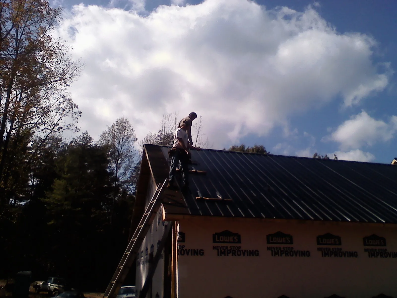 Roofer fastening dark metal panels high against a cloudy sky, from a Roof Inspection job in Millry